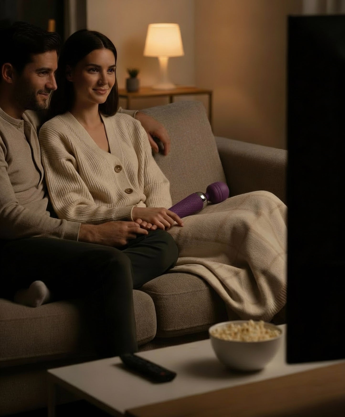 Couple relaxing on a sofa in a softly lit living room with a handheld wellness massager